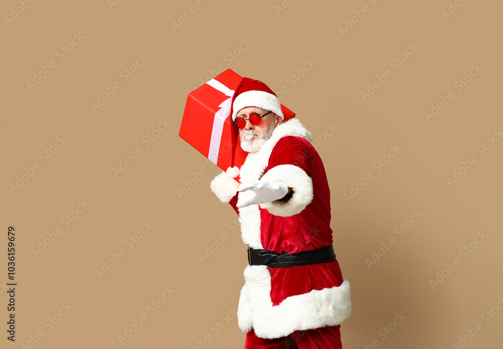 Santa Claus in sunglasses with gift box on brown background Santa Claus in sunglasses with gift box on brown background