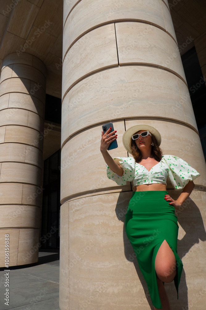 Beautiful tourist girl with hat holding mobile phone and talking at the city square.