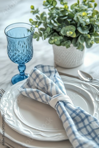 Elegant blue glass on a beautifully set dining table with a green plant by th...
