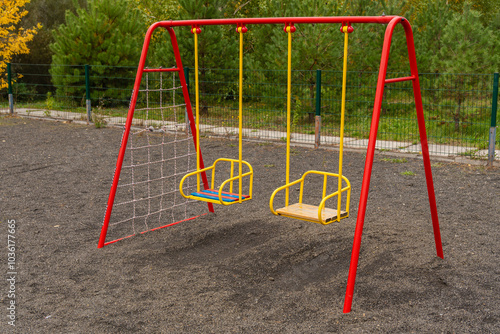 The playground features a bright red swing set with two seats, surrounded by a gravel area, perfect for children to enjoy swinging and outdoor playtime photo