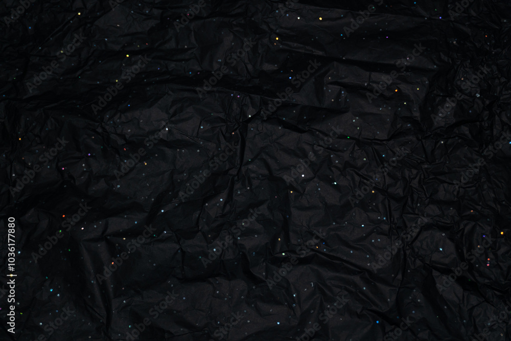 Black, crumpled wrapping paper with holographic fragments scattered across it. As light hits, the rainbow-like sparkles resemble distant stars in a vast, dark sky. Black, crumpled wrapping paper with holographic fragments scattered across it. As light hits, the rainbow-like sparkles resemble distant stars in a vast, dark sky.