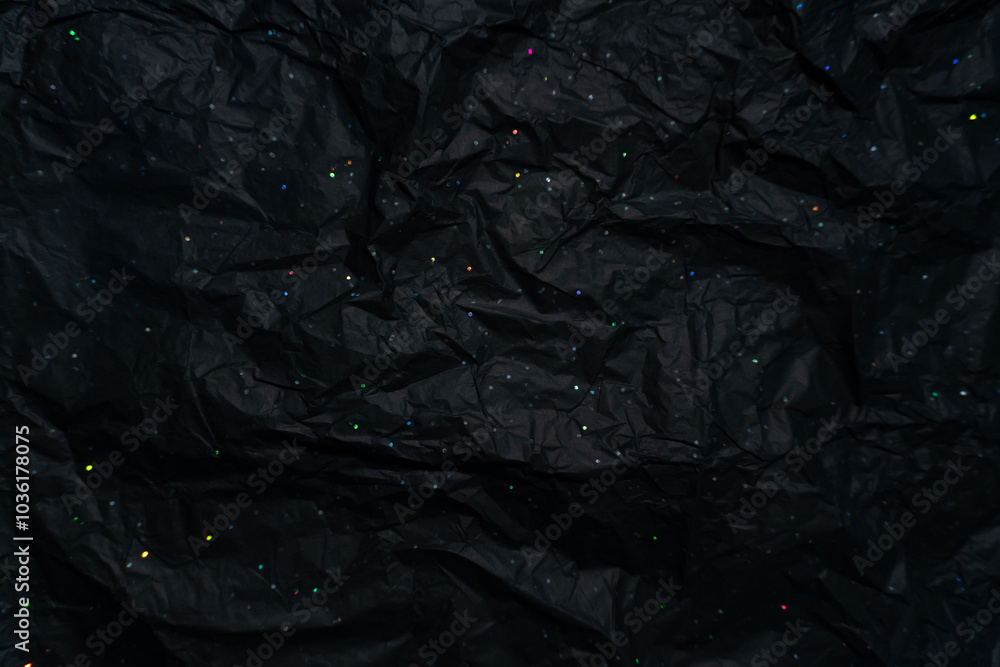 Crumpled black wrapping paper with holographic speckles, shimmering in all the colors of the rainbow under light. The texture and sparkle create a cosmic effect, reminiscent of a starry night sky. Crumpled black wrapping paper with holographic speckles, shimmering in all the colors of the rainbow under light. The texture and sparkle create a cosmic effect, reminiscent of a starry night sky.