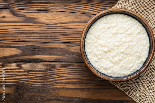 A bowl of simple porridge on a wooden table, with a burlap cloth beside it. The cottage cheese is creamy and textured, showcasing its curds. The wooden surface adds a rustic feel to the image.