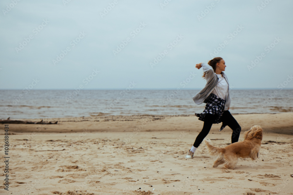 Girl throwing a ball for her dog on the beach, capturing a playful moment between the two. Casual autumn clothing, plaid shirt tied around her waist.