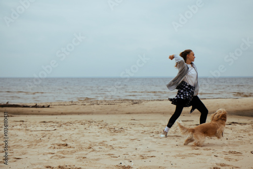Obraz na płótnie Girl throwing a ball for her dog on the beach, capturing a playful moment between the two. Casual autumn clothing, plaid shirt tied around her waist. w salonie