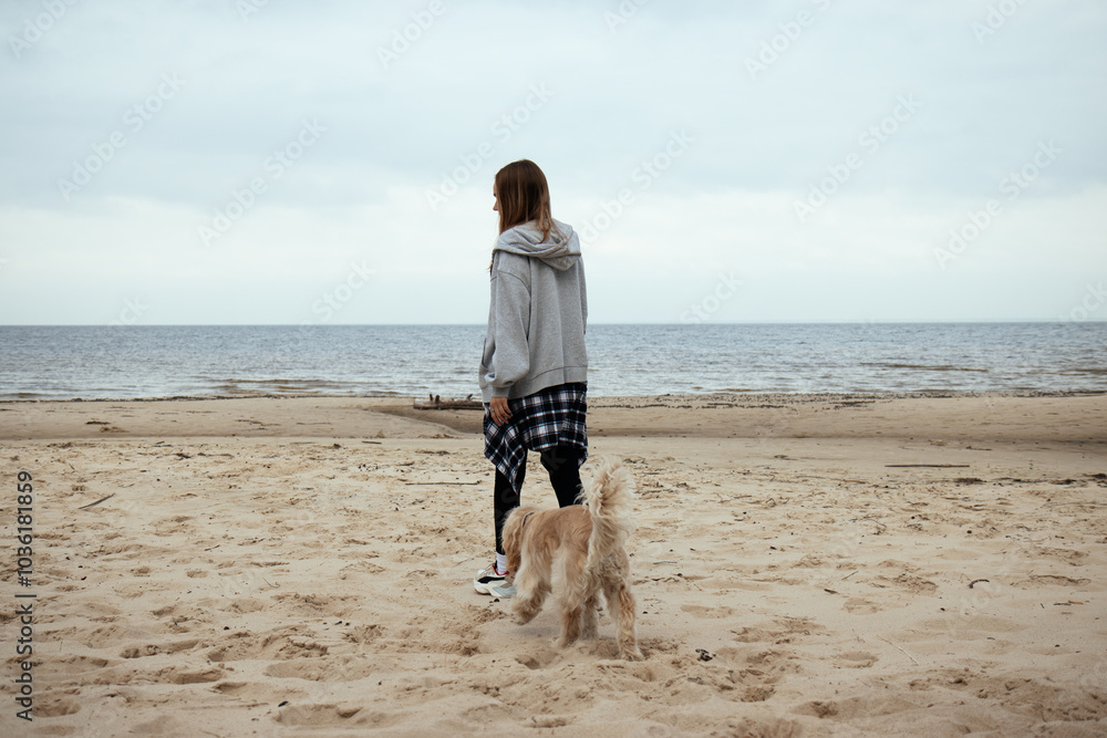 Beachside stroll with a dog as the autumn season sets in. The girl, in a casual outfit, enjoys the calm seaside atmosphere with her loyal pet by her side.