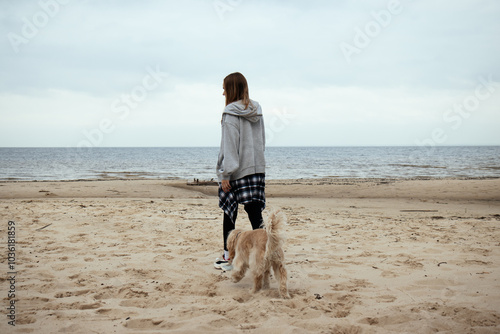 Obraz na płótnie Beachside stroll with a dog as the autumn season sets in. The girl, in a casual outfit, enjoys the calm seaside atmosphere with her loyal pet by her side. w salonie