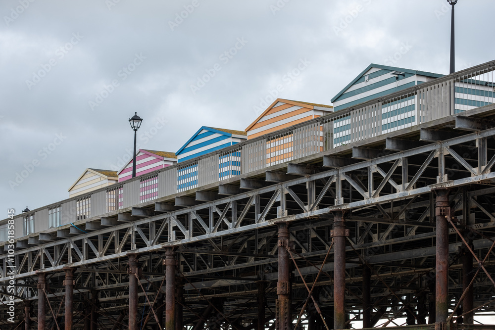 Colorful beach huts line the pier under a cloudy sky on a cool day by the seaside Colorful beach huts line the pier under a cloudy sky on a cool day by the seaside