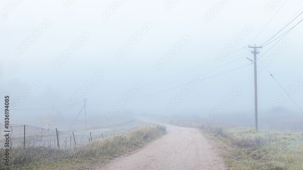 A rural dirt road stretches into the fog, with power lines running alongside, creating a quiet, atmospheric scene of rural life. A rural dirt road stretches into the fog, with power lines running alongside, creating a quiet, atmospheric scene of rural life.