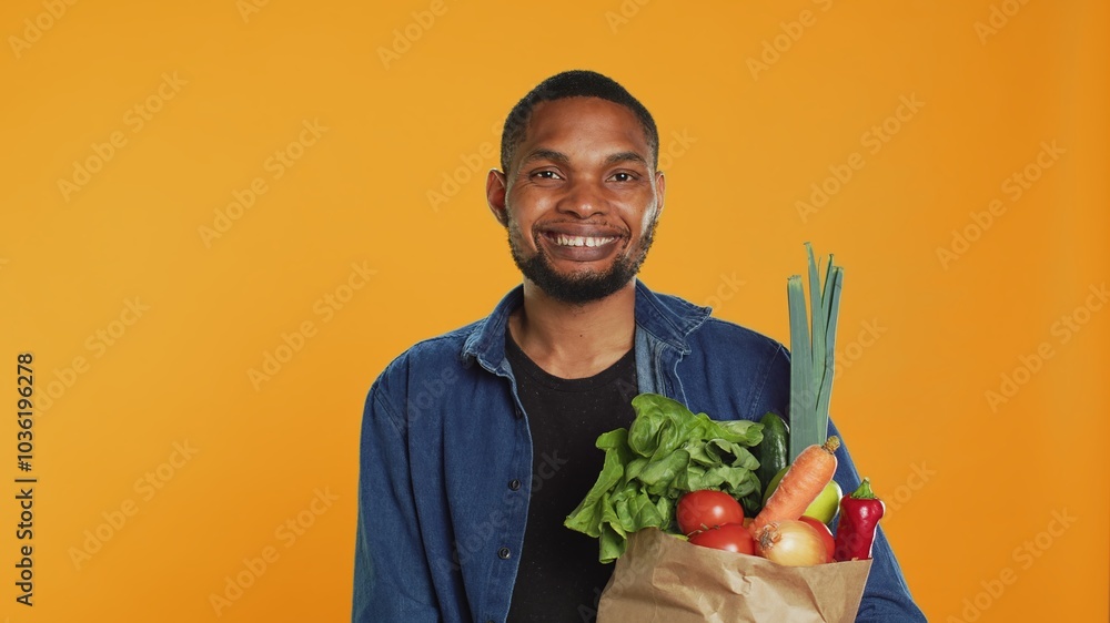 Portrait of african american guy posing with a paper bag full of groceries, shopping for organic ethically sourced goods. Vegan person supporting zero waste sustainable lifestyle. Camera A. Portrait of african american guy posing with a paper bag full of groceries, shopping for organic ethically sourced goods. Vegan person supporting zero waste sustainable lifestyle. Camera A.