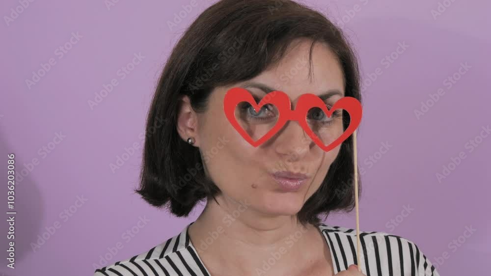 Portrait of a young cheerful woman putting on a carnival paper mask of heart-shaped glasses slow motion Portrait of a young cheerful woman putting on a carnival paper mask of heart-shaped glasses slow motion