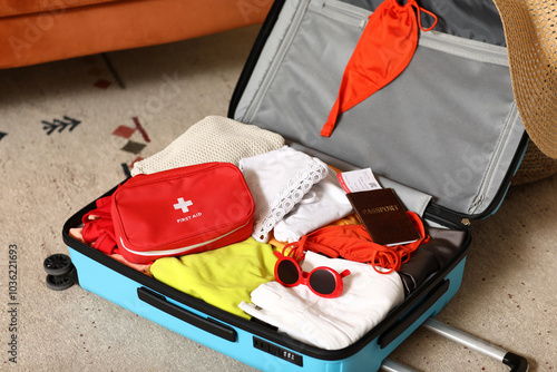 Suitcase with first aid kit, stylish clothes and passport on floor in room photo