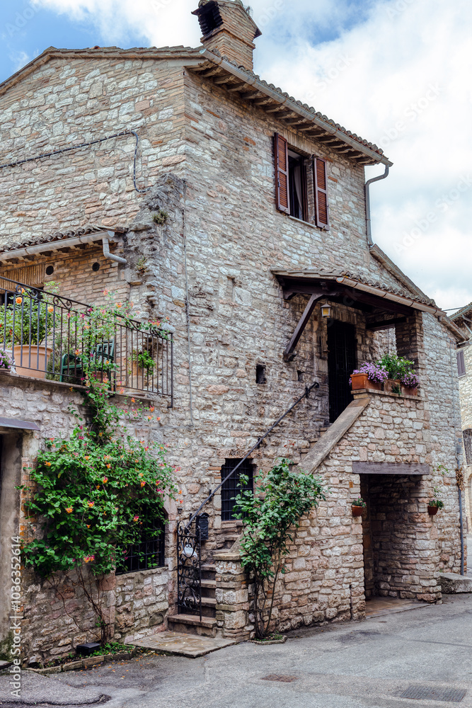 A charming cobblestone street in medieval Assisi, (Umbria, Italy), featuring ancient stone buildings and vibrant flower pots A charming cobblestone street in medieval Assisi, (Umbria, Italy), featuring ancient stone buildings and vibrant flower pots