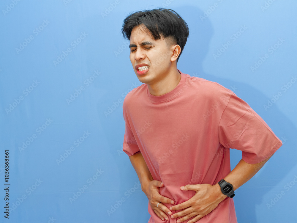 Unhealthy man pressing stomach, showing pain and sad expression, isolated on blue background. Suitable for health and lifestyle topics. Unhealthy man pressing stomach, showing pain and sad expression, isolated on blue background. Suitable for health and lifestyle topics.