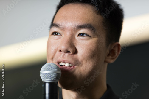 A closeup headshot of a young man giving a speech with a microphone photo