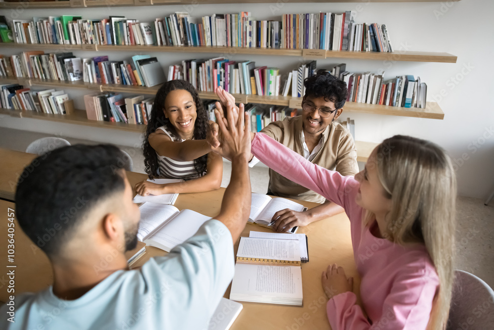 Multiethnic team of happy university students giving high five over open books on large table, meeting for successful teamwork in public library, enjoying group success, clapping hands, laughing Multiethnic team of happy university students giving high five over open books on large table, meeting for successful teamwork in public library, enjoying group success, clapping hands, laughing