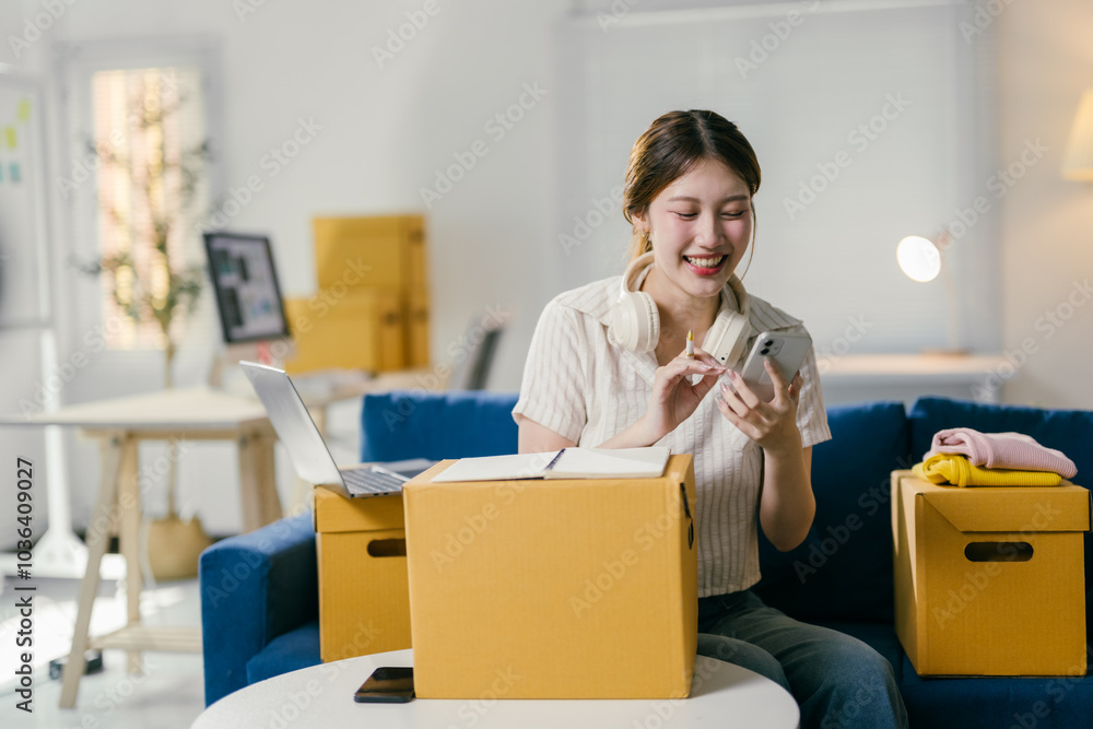 Entrepreneur is checking a sales order on her smartphone while sitting on a couch in her home office, surrounded by cardboard boxes and delivery packages Entrepreneur is checking a sales order on her smartphone while sitting on a couch in her home office, surrounded by cardboard boxes and delivery packages
