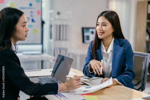 Two businesswomen are having a productive meeting in the office, analyzing financial charts and reports while working together on a project