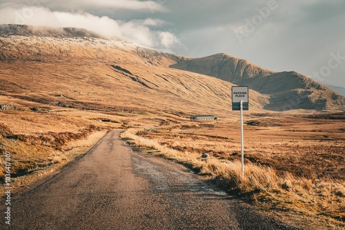 Scenic road passing through a mountainous landscape with a 'passing place' sign and a clear sky