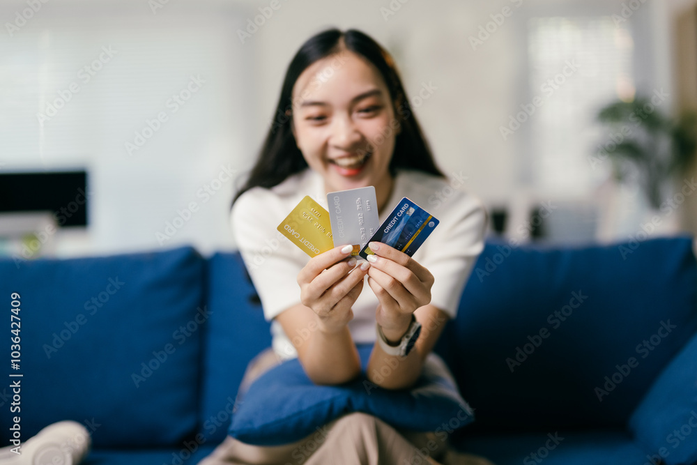 Young woman happily shops online from her home, holding three credit cards with a smile, embodying a modern lifestyle of digital banking and consumerism Young woman happily shops online from her home, holding three credit cards with a smile, embodying a modern lifestyle of digital banking and consumerism