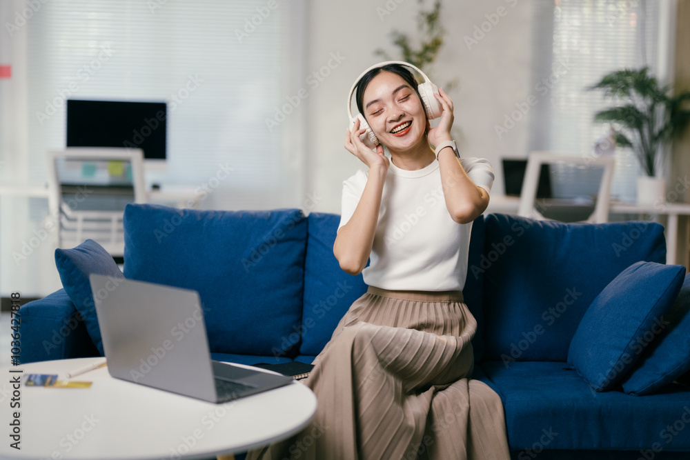 Content freelancer is taking a break on a cozy blue couch, lost in her favorite song playing through her headphones. She looks relaxed and happy, enjoying the music in her home office