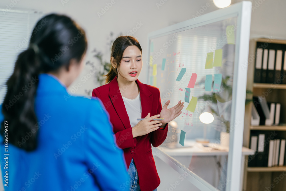 Young asian businesswoman is leading a brainstorming session with her team, using adhesive notes on a glass wall to organize ideas Young asian businesswoman is leading a brainstorming session with her team, using adhesive notes on a glass wall to organize ideas