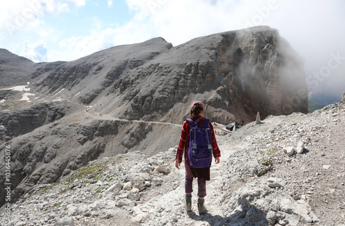 woman walks with backpack on shoulders in rugged path of stony mountain in European Alps in summer photo