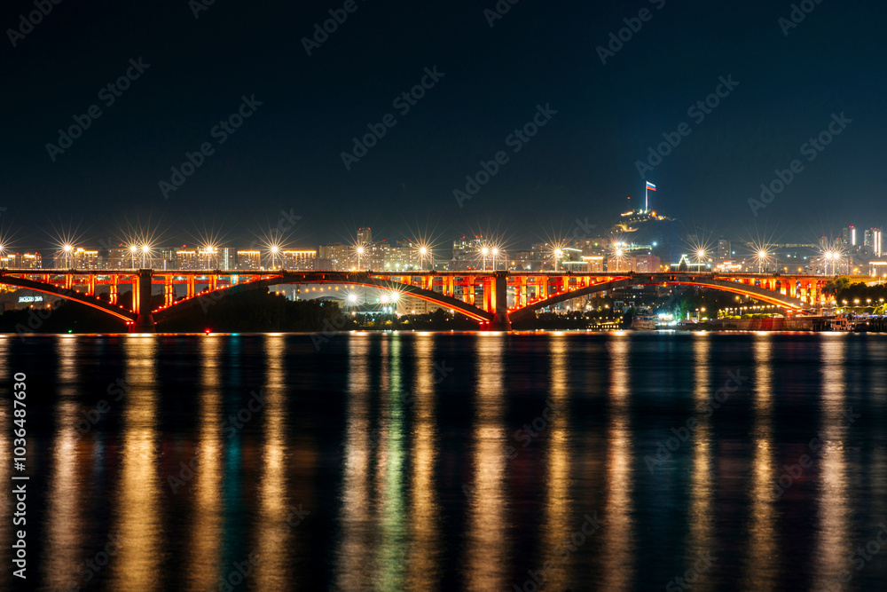 Communal bridge over the Yenisei River at night with beautiful lighting and reflection in the water Communal bridge over the Yenisei River at night with beautiful lighting and reflection in the water