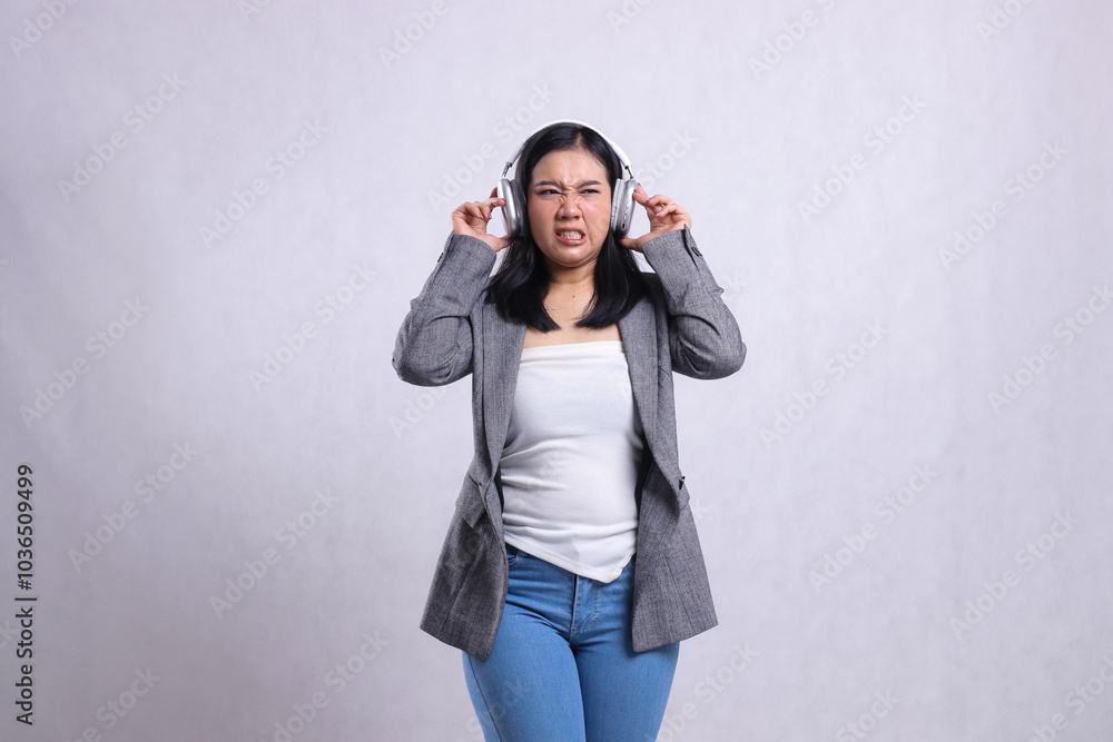 beautiful young office ladies disgusted holding and wearing headphone headset listening music wearing grey suit isolated on white background. lifestyle concept, advertising, entertainment, technology beautiful young office ladies disgusted holding and wearing headphone headset listening music wearing grey suit isolated on white background. lifestyle concept, advertising, entertainment, technology