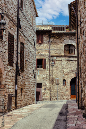 A winding alleyway in the medieval town of Assisi, Umbria, showcasing historic stone architecture under a bright sky. Assisi, Italy,