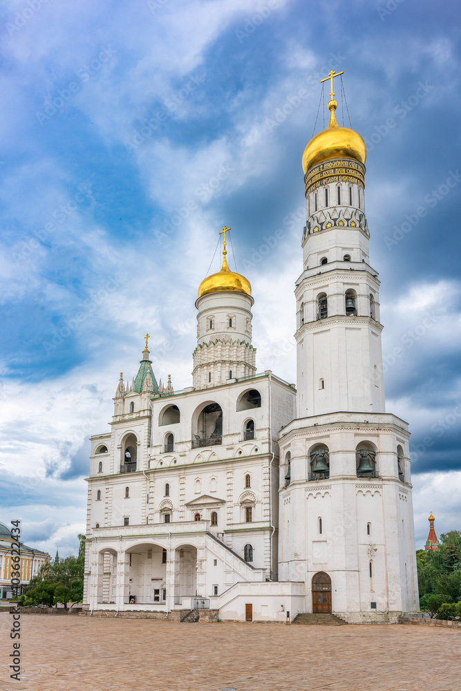 Ivan the Great Bell Tower, with Assumption Belfry on the right in Moscow Kremlin. Blue sky background with sunbeams Ivan the Great Bell Tower, with Assumption Belfry on the right in Moscow Kremlin. Blue sky background with sunbeams