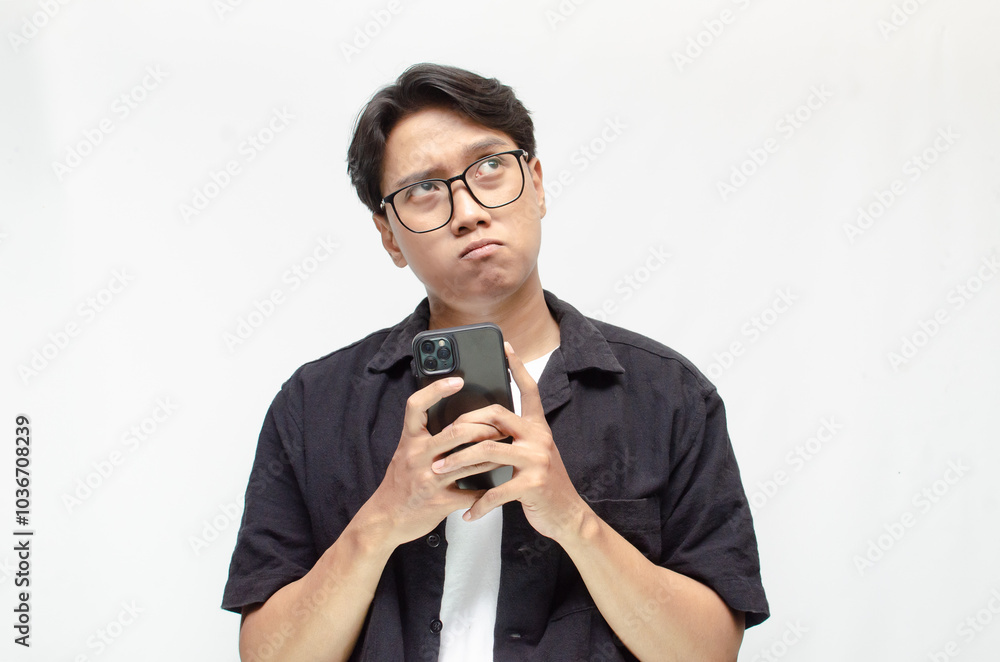 a sad and overthinking young Asian man in a pensive mood holding a phone with a sad and thoughtful expression. Asian man holding phone while questioning, wondering and crying. a sad and overthinking young Asian man in a pensive mood holding a phone with a sad and thoughtful expression. Asian man holding phone while questioning, wondering and crying.