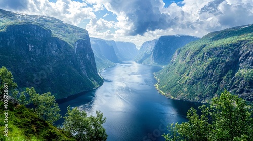 A scenic view of a fjord with steep, green mountains on either side. The water is calm and blue, reflecting the sunlight.