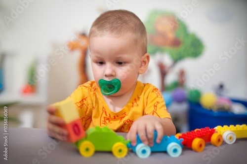 Young child explores colorful building blocks while playing with a train set in a bright indoor play area