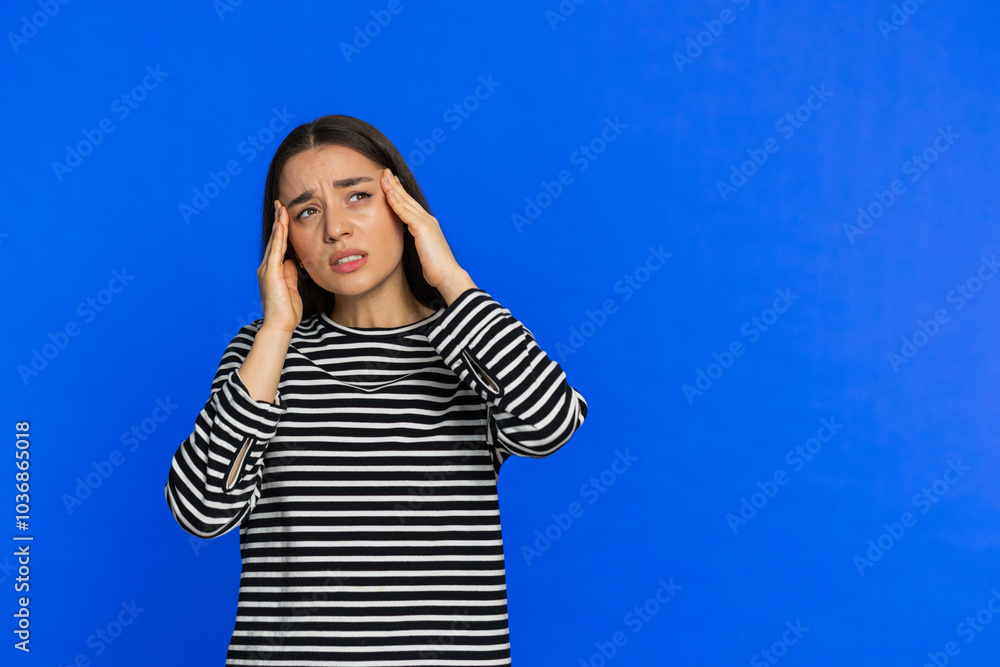 Exhausted young woman girl rubbing temples to cure headache problem, suffering from tension, migraine stress, grimacing in pain, high blood pressure isolated alone on blue wall background. Copy-space Exhausted young woman girl rubbing temples to cure headache problem, suffering from tension, migraine stress, grimacing in pain, high blood pressure isolated alone on blue wall background. Copy-space