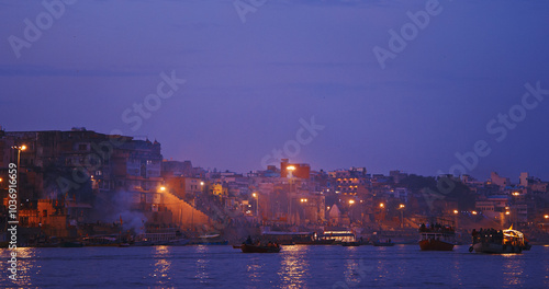 Obraz na płótnie Varanasi, Uttar Pradesh, India. Funeral rites of cremation at the Harishchandra Ghat. Evening pink purple sunset sky, night time. Camera moving along riverbank embankment. Cinematic View from boat w salonie