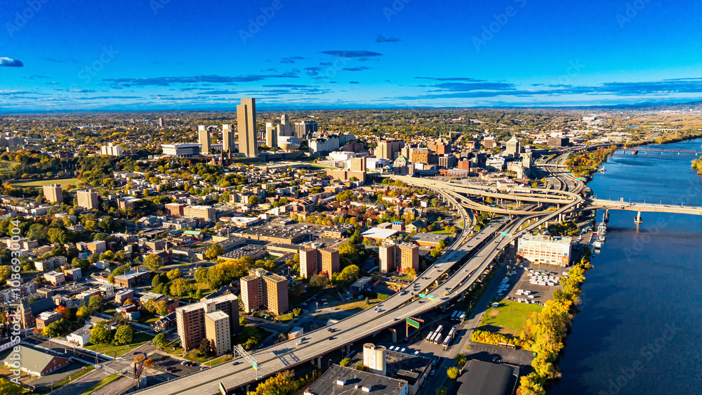Obraz premium Aerial view of Albany during a clear sunny day. The skyline of Albany showcases vibrant city life with buildings, roads, and a serene river under a bright blue sky.