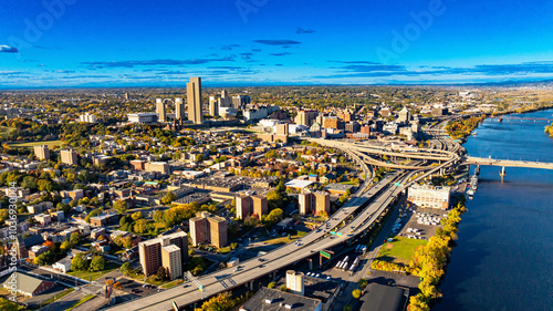 Aerial view of Albany during a clear sunny day. The skyline of Albany showcases vibrant city life with buildings, roads, and a serene river under a bright blue sky. photo