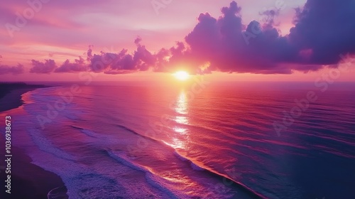 Aerial view of a vibrant sunset sky with beautiful light over the sea featuring colorful clouds and dramatic waves reflecting purple hues in the background