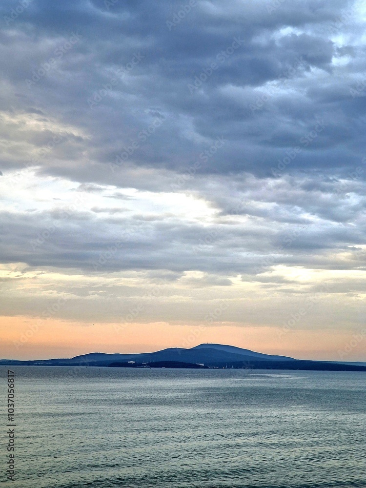 Setting sun over the horizon with a view of the sea and mountains.