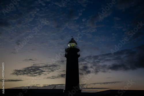 Lighthouse shining at sunset with cloudy sky photo