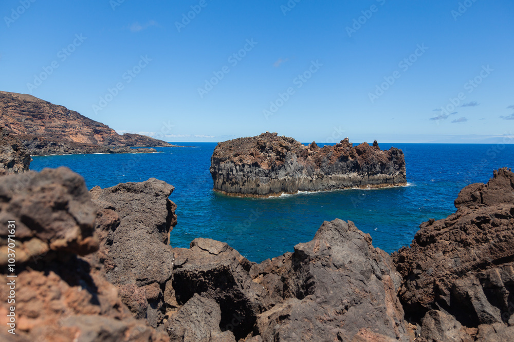 Volcanic rocks are surrounding a small island in the ocean Volcanic rocks are surrounding a small island in the ocean
