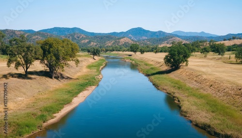 A serene river flows through a landscape of hills and dry grass under a clear sky.