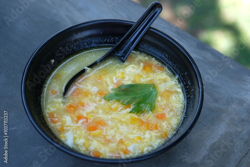 corn soup in a black bowl. sop jagung. sweet corn, chicken meat, carrots, celery, eggs, spices. photo