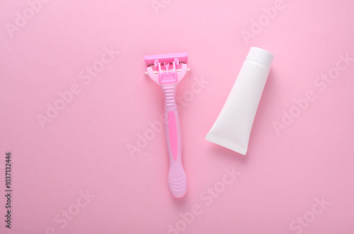 Razor with cream tube on pink background