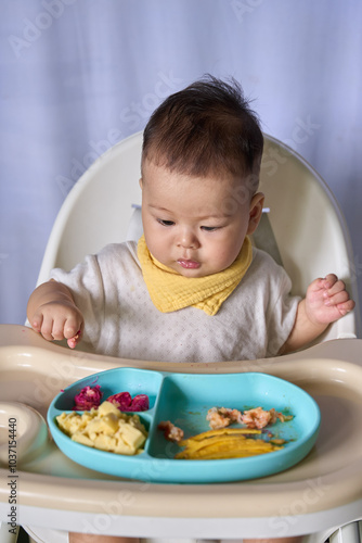 9 month old Asian baby boy is learning to eat, with food on the table, the baby eats and commands himself, it seems a bit messy