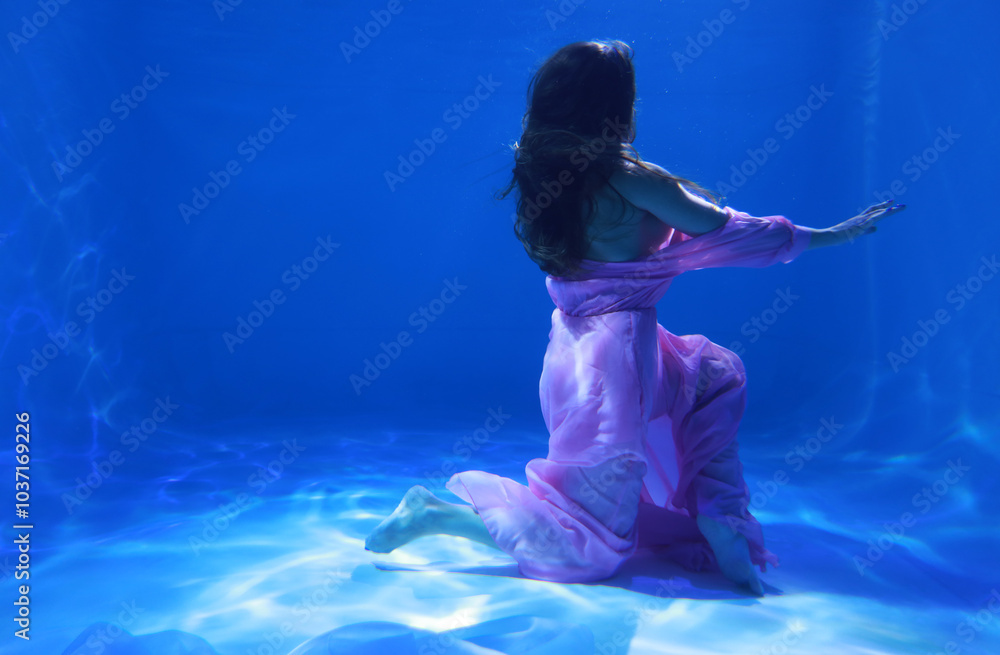 Woman in pink dress dancing underwater in the pool in blue light Woman in pink dress dancing underwater in the pool in blue light