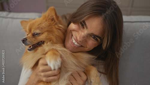 A smiling young woman embraces her pomeranian dog in a cozy indoor living room setting.