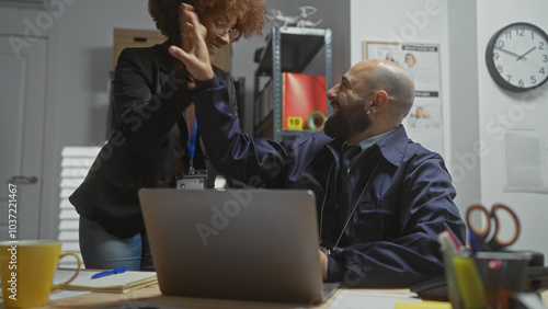 A woman and a man celebrate success with a high-five in a modern police station office, indicating teamwork and job satisfaction. photo