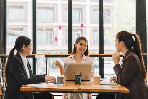 Collaborative business meeting with three women discussing ideas at modern office table. They are engaged and smiling, showcasing teamwork and communication
